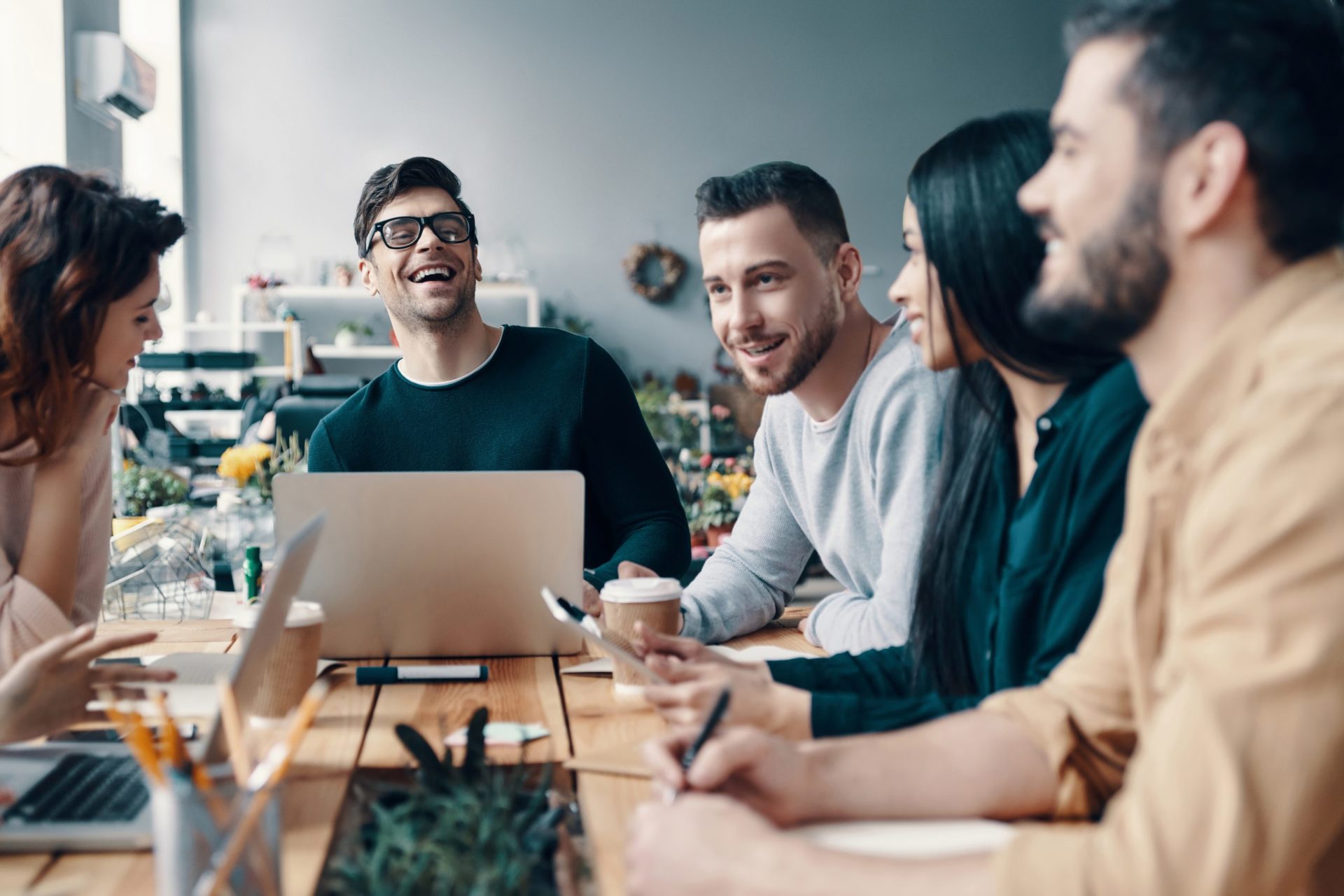 Happy to work together. Group of young modern people in smart casual wear discussing something and smiling while working in the creative office positive culture